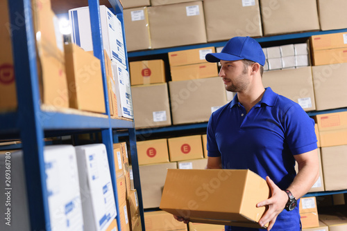 Portrait of delivery staff in blue uniform work in warehouse hold a parcel box keep goods and parcel organized © stnazkul