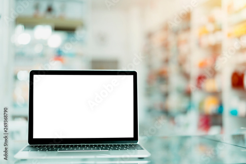 Laptop with blank screen on table with Pharmacy blurred with store drugs shelves interior background. pharmacist and chemist, middle east or transcontinental region centered on western Asia Concept