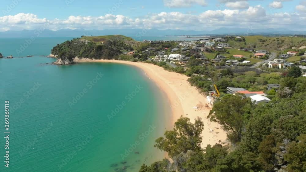 drone flying down past trees to a golden beach adjacent to a bay of turquoise blue water drone flying down past trees to a golden beach adjacent to a bay of turquoise blue water