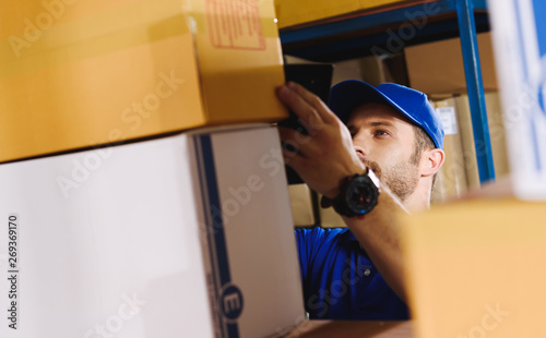 Fotografie Portrait of delivery staff in blue uniform looking for particular box in warehou