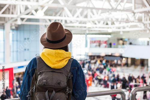 Young female traveller in hat with backpack over modern airport interior