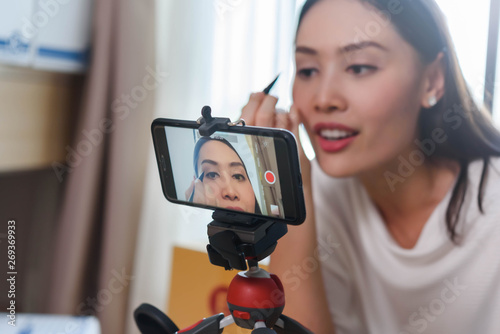 Beauty blogger demonstrating how to apply eyeliner and review products on live broadcast for social media by smartphone, life of an influencer