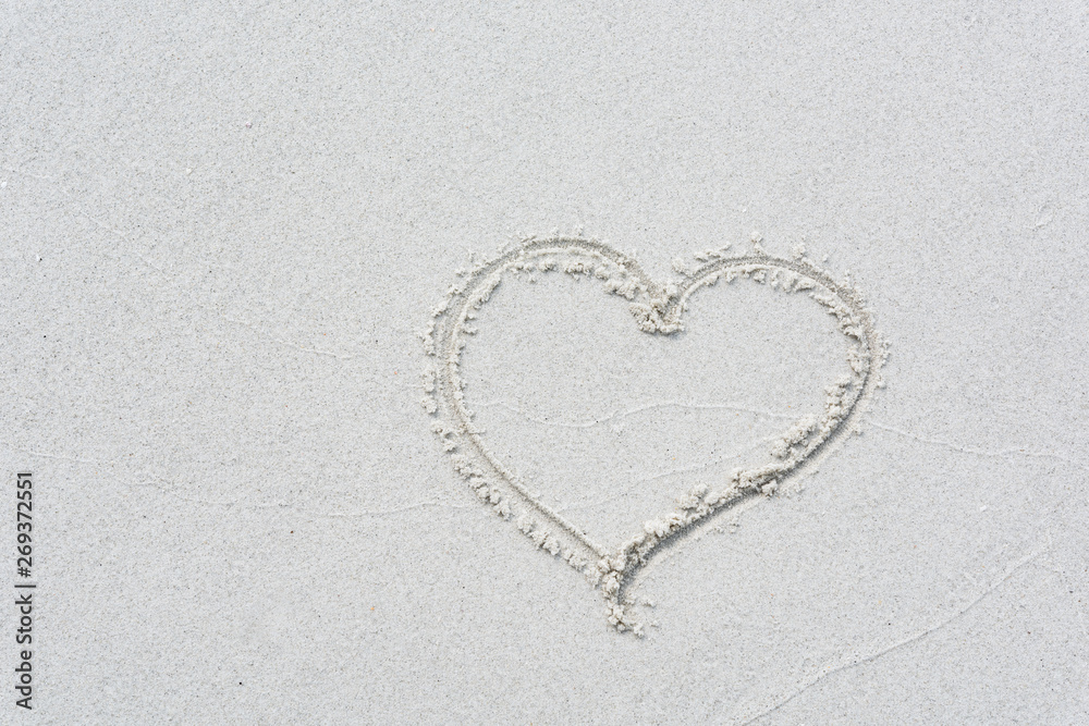 Drawn love heart shape on white sand beach background