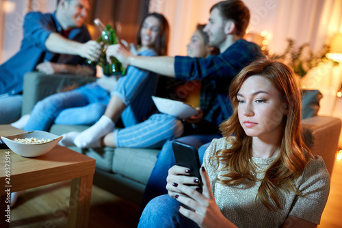 technology, internet addiction and people concept - sad young woman with smartphone at home friends party in evening