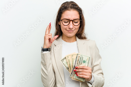 Young european business woman holding dollar banknotes crossing fingers for having luck photo