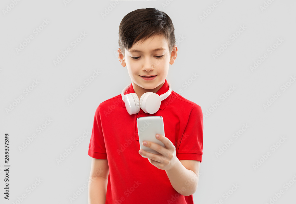 technology, childhood and people concept - smiling little boy in red polo t-shirt with headphones on neck using smartphone over grey background technology, childhood and people concept - smiling little boy in red polo t-shirt with headphones on neck using smartphone over grey background