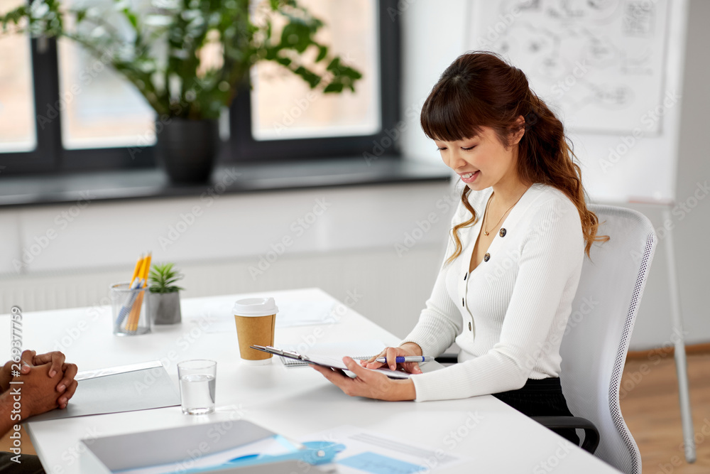 new job, business and employment concept - smiling asian female employer or hr manager with clipboard having interview with male employee at office new job, business and employment concept - smiling asian female employer or hr manager with clipboard having interview with male employee at office