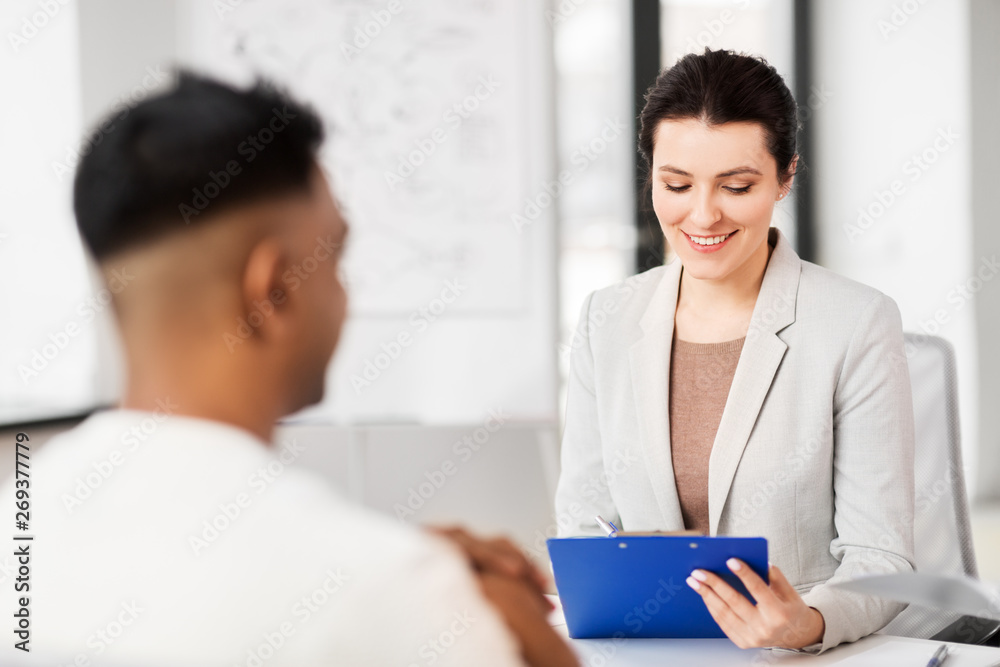 job, business and employment concept - smiling female employer or hr manager with clipboard having interview with male employee at office job, business and employment concept - smiling female employer or hr manager with clipboard having interview with male employee at office
