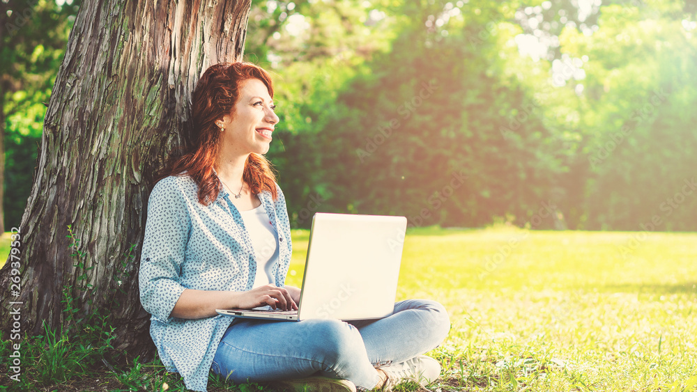 Smiling young girl making notes in notepad while sitting outdoors with laptop computer