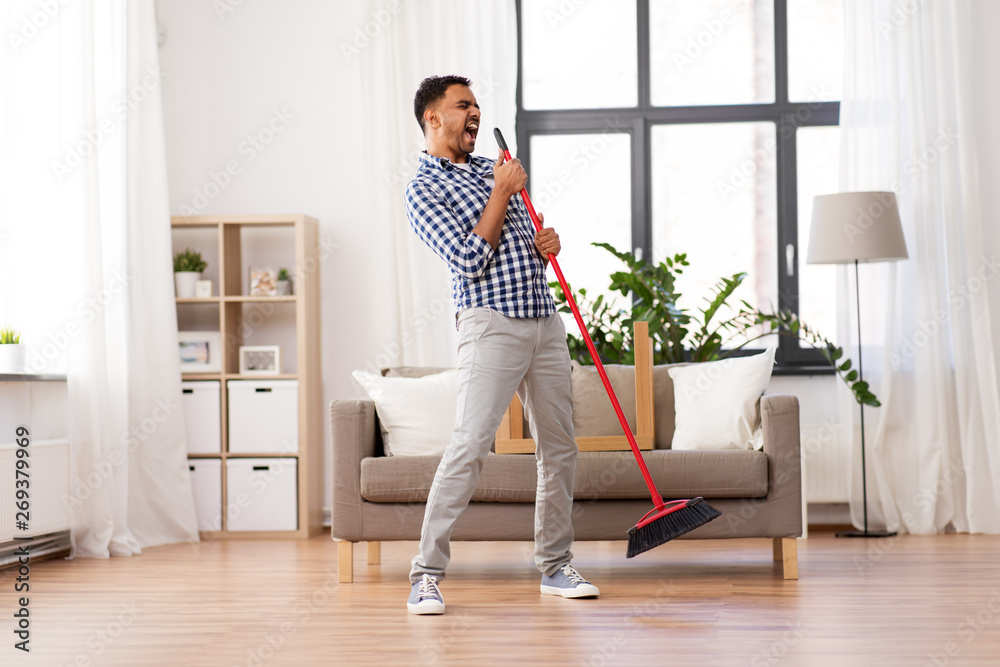 cleaning, housework and housekeeping concept - indian man with broom sweeping floor and singing at home cleaning, housework and housekeeping concept - indian man with broom sweeping floor and singing at home