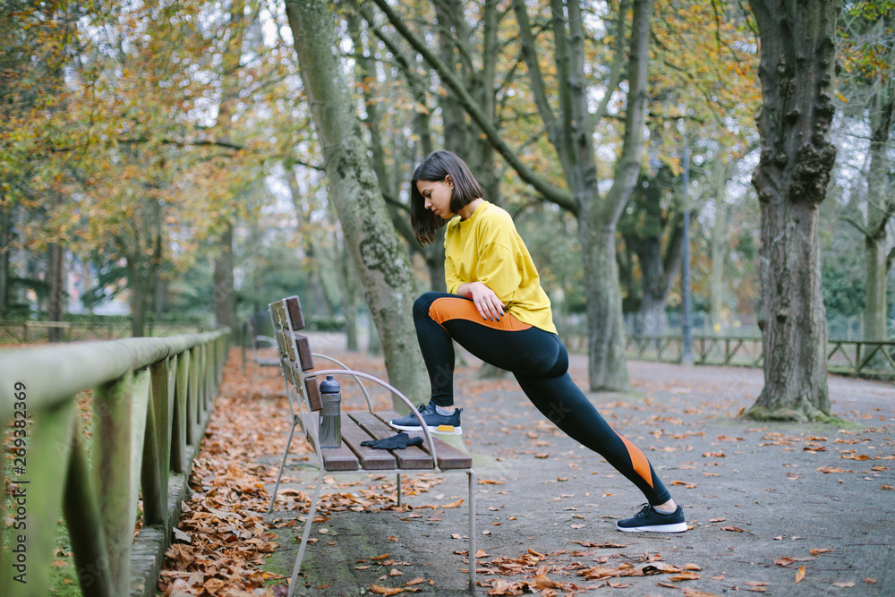 Female athlete stretching for warming up before running at city park in autumn. Sporty woman exercising outdoor.