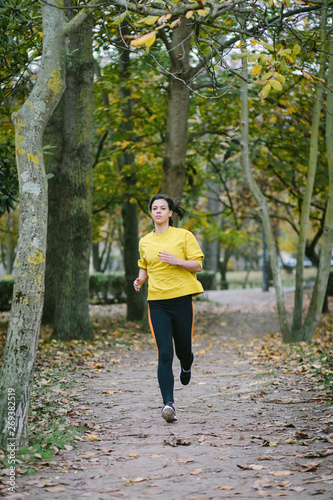 Sporty woman running in place at city park in autumn. Female athlete exercising outdoor.