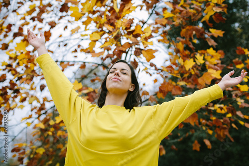 Sporty young woman relaxing and breathing in autumn under a tree. Tranquility and relax in fall season.