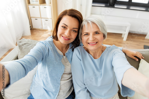 family, generation and people concept - portrait of senior mother and adult daughter taking selfie at home