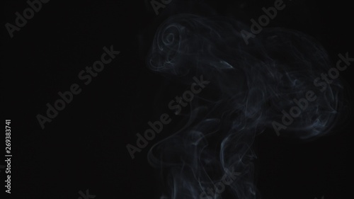 Thin trickle of gray smoke slowly rising graceful twists up on black background. Black and white smoke blowing from bottom to top