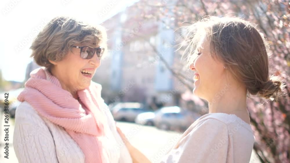Talking mother and adult daughter on the street in the spring. Bright morning sun, mother's day, daughters day Talking mother and adult daughter on the street in the spring. Bright morning sun, mother's day, daughters day