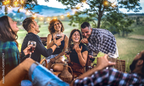 Young friends having fun at vineyard after sunset - Happy people millennial camping at open air pic nic under bulb lights - Youth friendship concept with guys and girls drinking wine at barbeque party photo