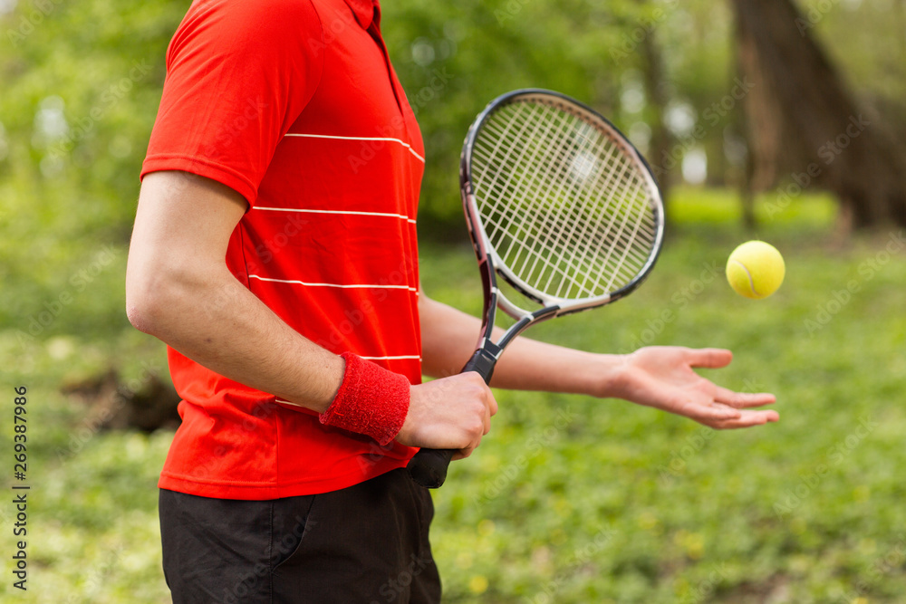 Close up of men's hands hold a tennis racket and ball on the green background. Sport concept