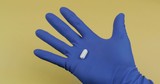 One oval white pill in hand dressed in rubber sterile medical glove