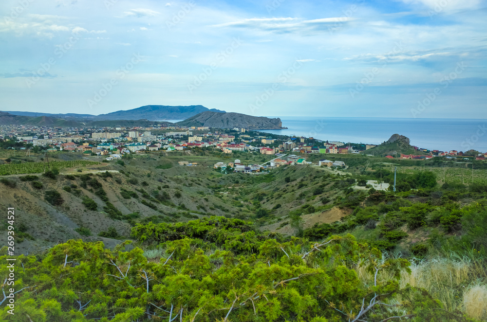 Crimean Republic, Russia - May 30, 2017: View of the Sudak district, residential buildings, rolling hills, vineyards, sea on the horizon.