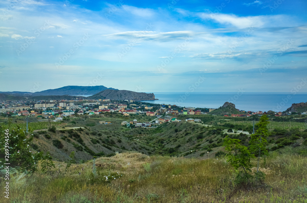 Sudak, Crimean Republic, Russia - May 30, 2017: View of the Sudak district, residential buildings, rolling hills, vineyards, sea on the horizon.