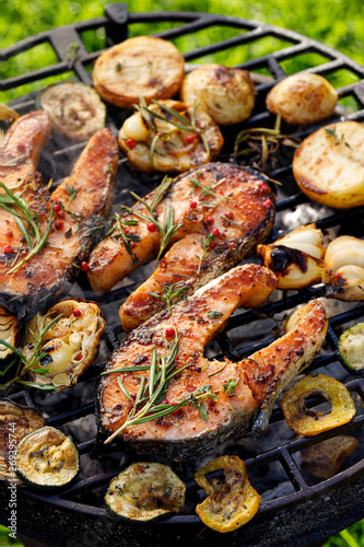 Grilled fish, grilled salmon steak with the addition of rosemary, aromatic spices and vegetables on the grill plate outdoors, top view, close-up. Grilled seafood