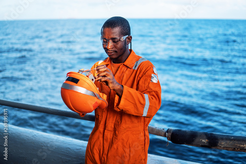 happy Seaman AB or Bosun on deck of vessel or ship , wearing PPE personal protective equipment - helmet, coverall, lifejacket, goggles. Safety at sea © Igor Kardasov