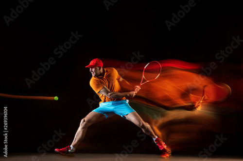 One caucasian man playing tennis isolated on black background in mixed light. Studio shot of fit young male player in motion or action during sport game. Concept of movement, sport, healthy lifestyle. © master1305