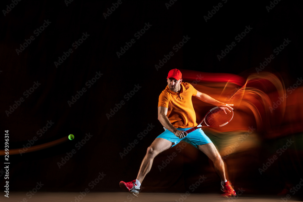 One caucasian man playing tennis isolated on black background in mixed light. Studio shot of fit young male player in motion or action during sport game. Concept of movement, sport, healthy lifestyle.