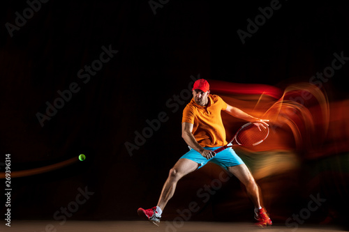 One caucasian man playing tennis isolated on black background in mixed light. Studio shot of fit young male player in motion or action during sport game. Concept of movement, sport, healthy lifestyle.