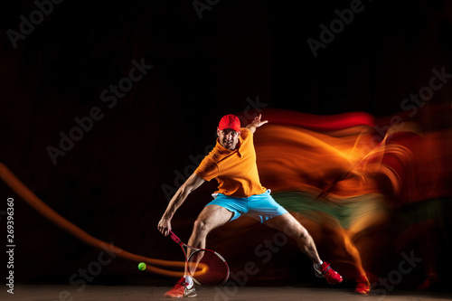One caucasian man playing tennis isolated on black background in mixed light. Studio shot of fit young male player in motion or action during sport game. Concept of movement, sport, healthy lifestyle.