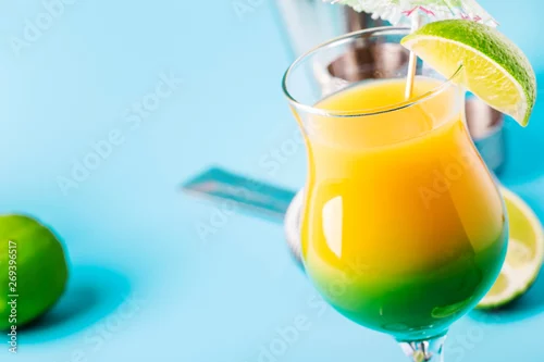 Obraz Dwuwarstwowy koktajl alkoholowy z sokiem mango, rumem, likierem, limonką i lodem, letnie niebieskie tło, miejsce na tekst