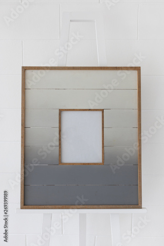 plank wooden picture frame on drawing easel with white brick wall background.