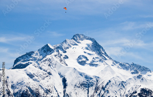 two parachutes flying in paralell in the sky over a snowed peak