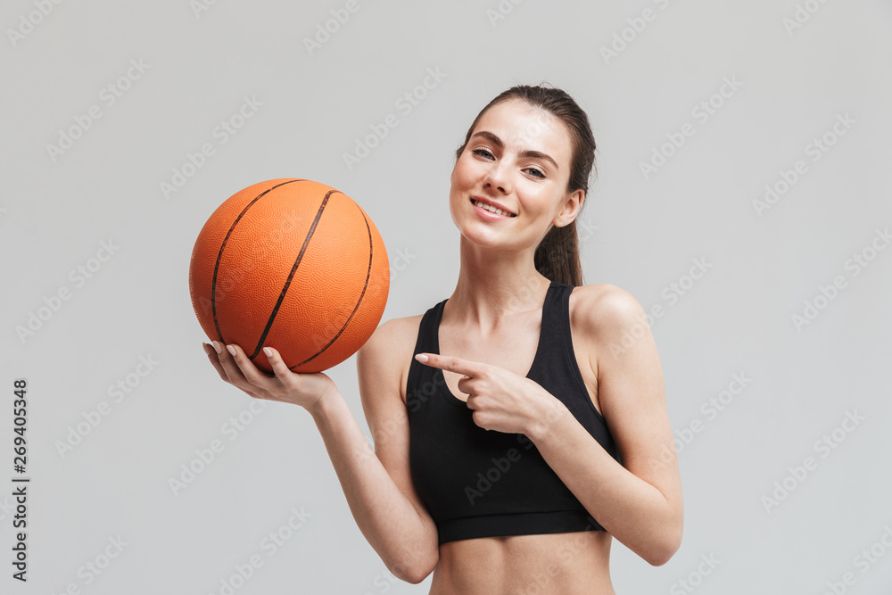 Sport fitness woman basketball player posing with basketball isolated over grey wall background.