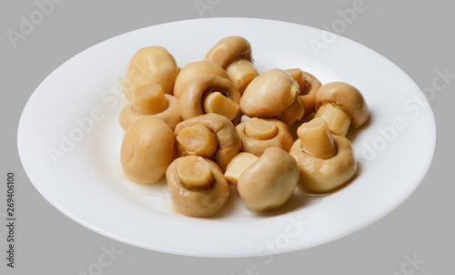 Marinated champignons on a white round plate. Light gray isolated background. Top side view. Close-up.