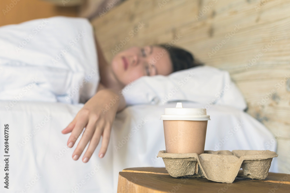 .A paper cup of coffee standing on the table in the bedroom in the early morning as a surprise for a sleeping .A paper cup of coffee standing on the table in the bedroom in the early morning as a surprise for a sleeping