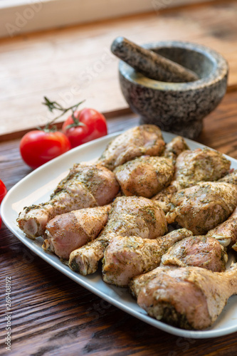 Raw chicken legs with herbs and spices on white dish.