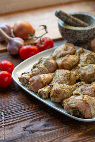 Raw chicken legs with herbs and spices on white dish.