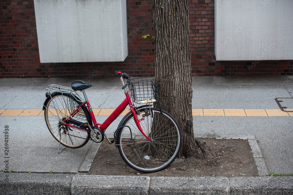 Red bicycle parking unattended near a tree on the sidewalk in Japan in the morning. Red bicycle parking unattended near a tree on the sidewalk in Japan in the morning.