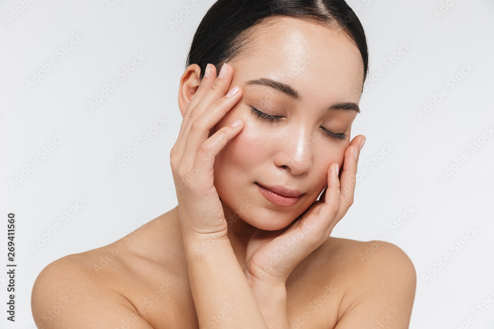 Portrait of tranquil half naked asian woman touching her clear skin with her eyes closed Portrait of tranquil half naked asian woman touching her clear skin with her eyes closed