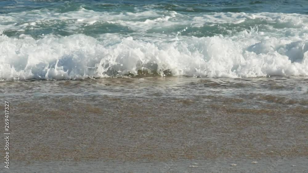 Close up low angle shot of waves breaking on sandy beach on sunny day in summer Close up low angle shot of waves breaking on sandy beach on sunny day in summer
