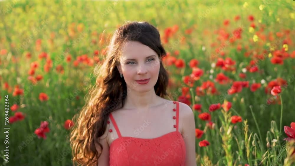 Close up, slow motion, portrait of an attractive woman in a red sundress with hair developing in the wind on the poppy field Close up, slow motion, portrait of an attractive woman in a red sundress with hair developing in the wind on the poppy field