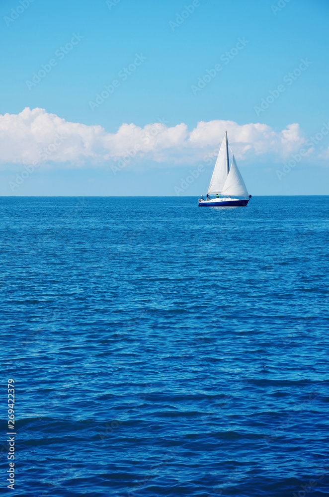 Blue sea water and a white sailboat.