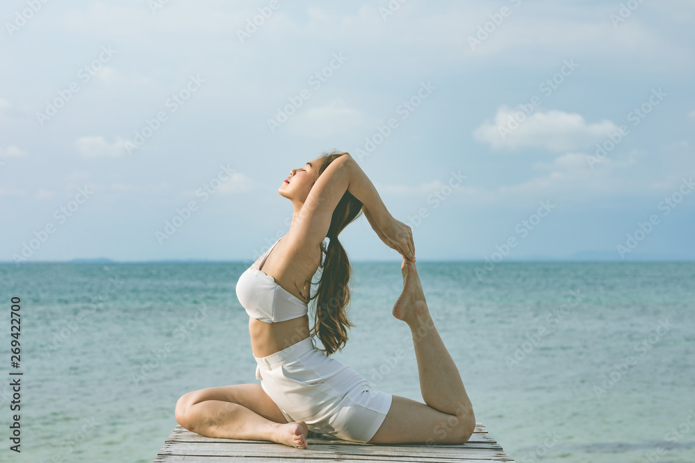 Vacation of Attractive Asian woman relaxing in yoga king pigeon pose on the pier above the beach with beautiful sea in Tropical island,Feeling comfortable and relax in holiday,Vacations Concept