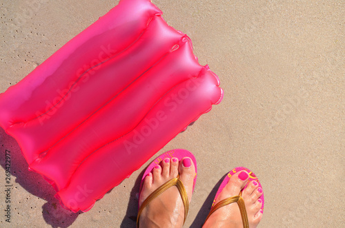 Background with an inflatable pillow and feet in a slaps on the sand.
