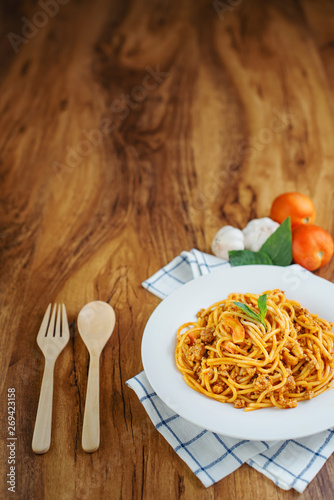 Spaghetti with tomato sauce in a white plate on a wooden background.