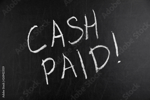 Words Cash Paid written by hand in white chalk on a blackboard