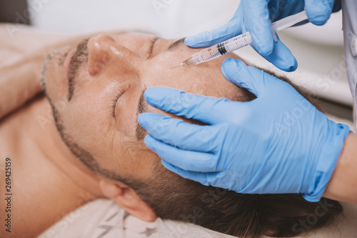 Mature man receiving facial filler injections by professional cosmetologist. Mid-aged man getting anti-wrinkle treatment at beauty salon. Botox, disport filler concept