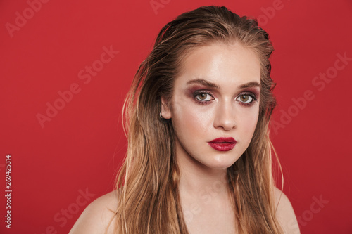 Beautiful young amazing woman with bright makeup red lipstick posing isolated over red wall background.